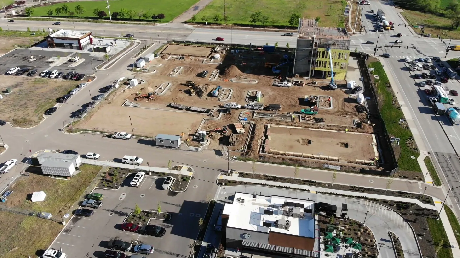 Aerial view of foundations being poured at the Arête site, framing wrapped in green, equipment on site — April 22, 2026