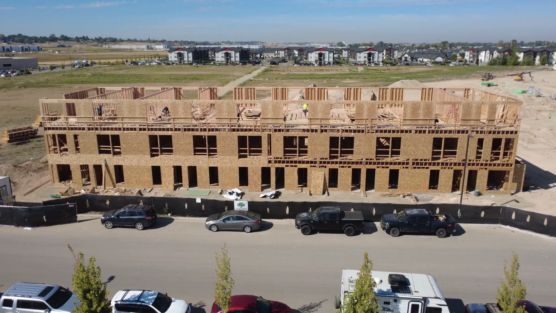 Aerial view of Arête townhome Buildings A and B in September 2026, framed to full three stories in wood with window and door openings cut into the walls